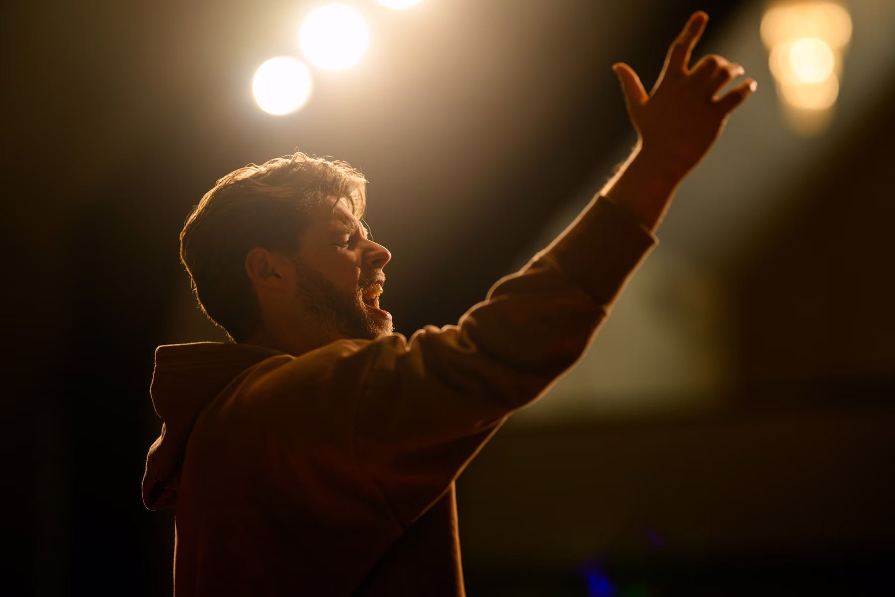 A close side view of Alex raising his hand toward warm overhead light.