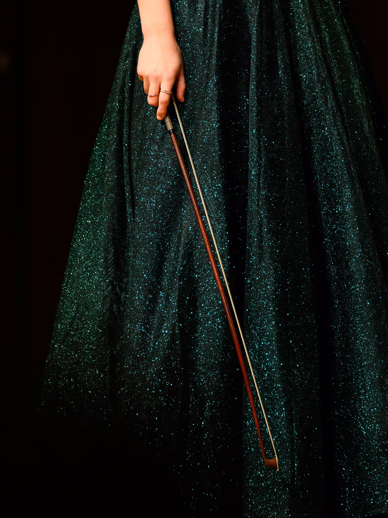 Detail of a violin bow held against a shimmering green gown.