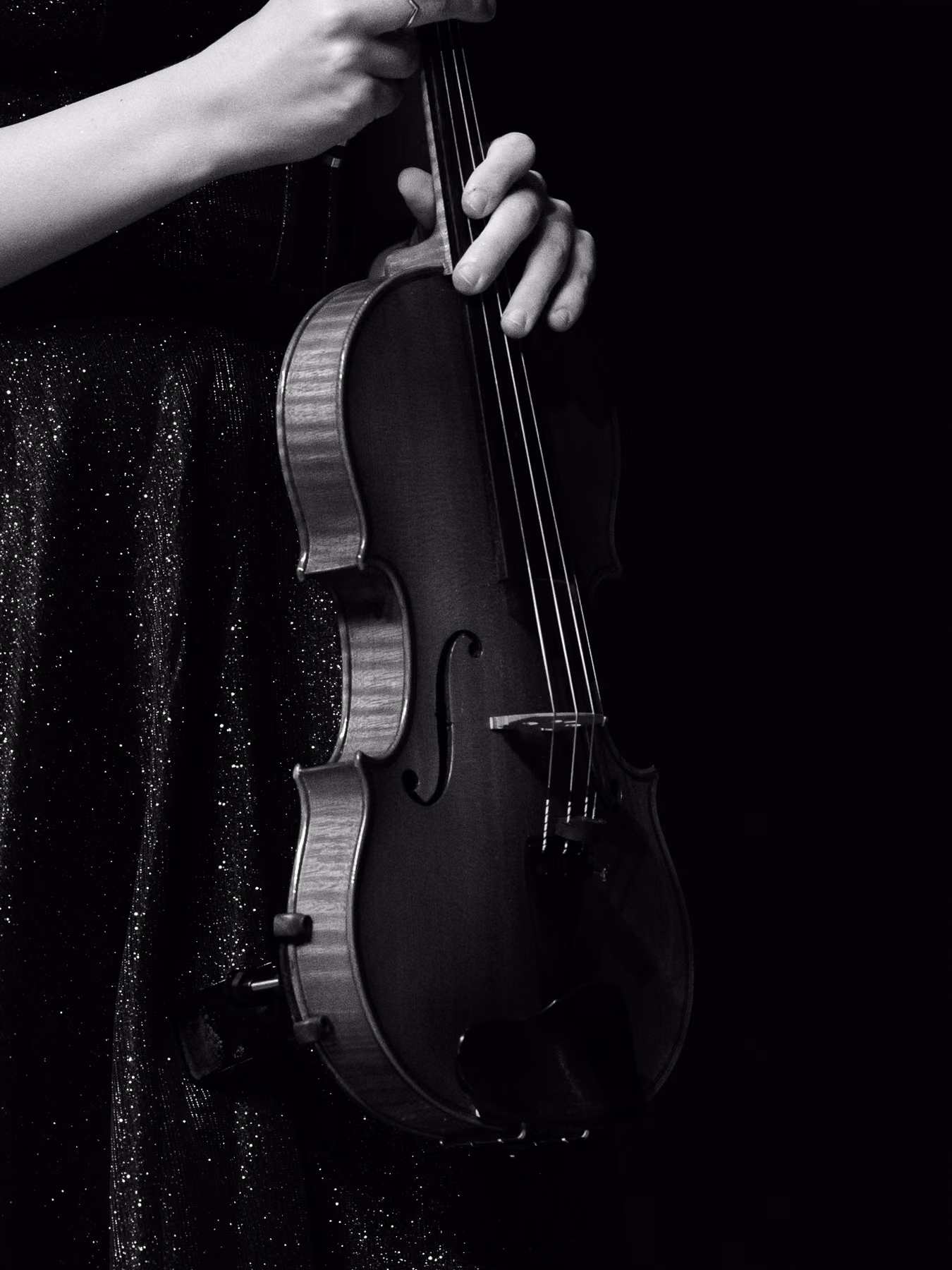 Black-and-white detail of a violin resting beside the performer’s hand.