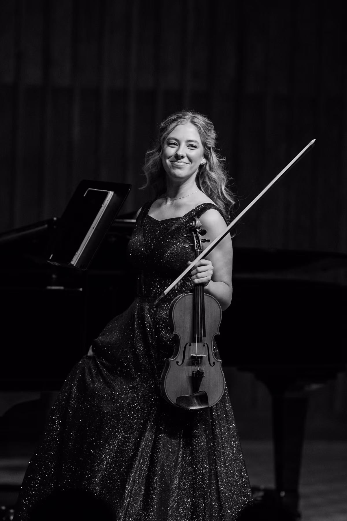 Alyssa smiling on stage with her violin and bow, in black and white.