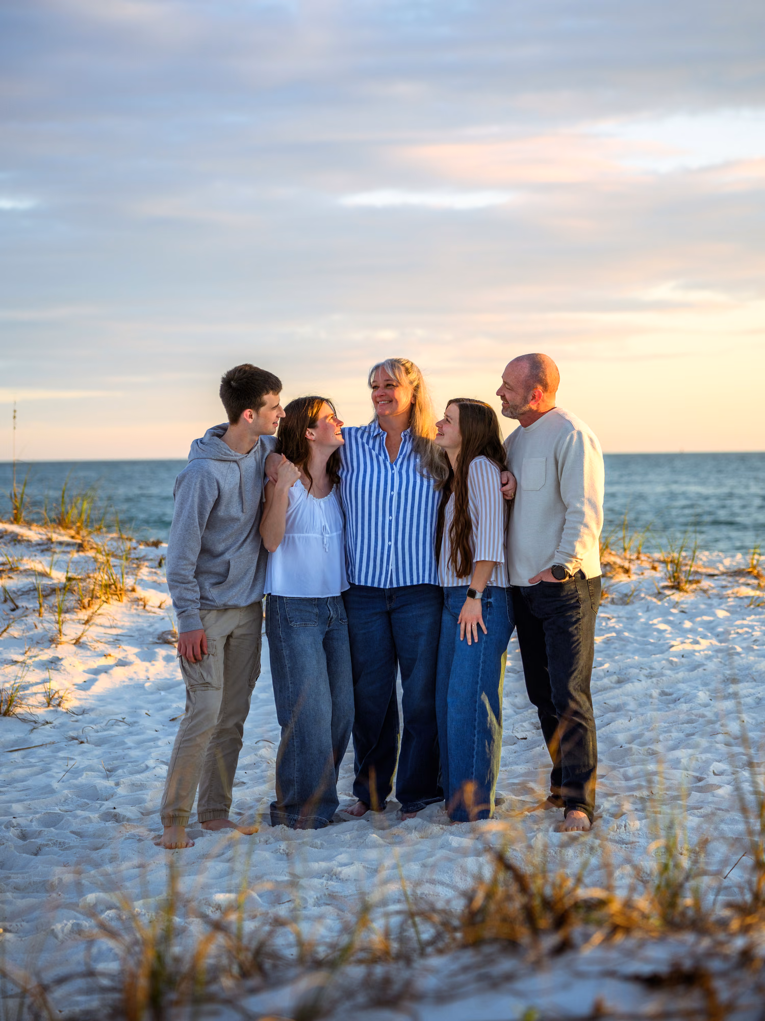A family of five stands close together on a beach, smiling toward one another in the evening light.