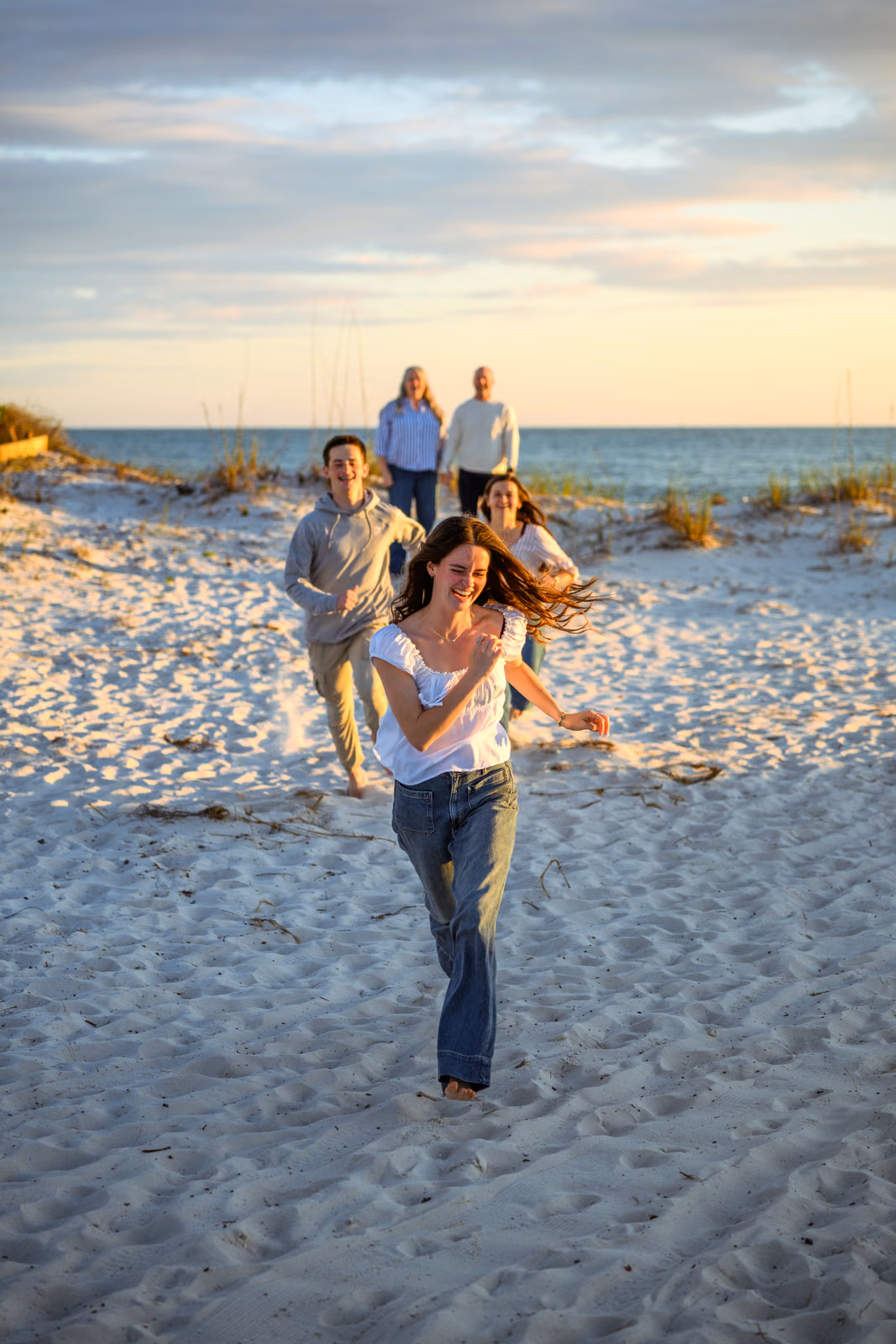 Three family members run toward the camera across the sand while two others watch behind them.
