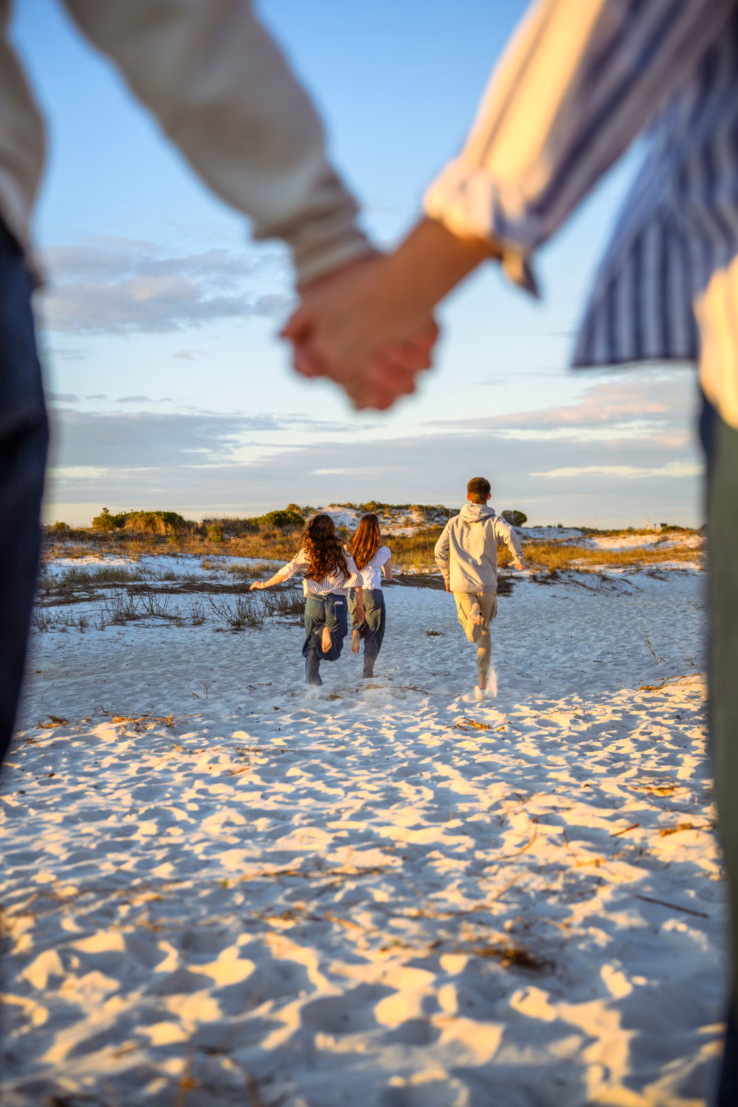 Clasped hands frame three family members running away across the sand.