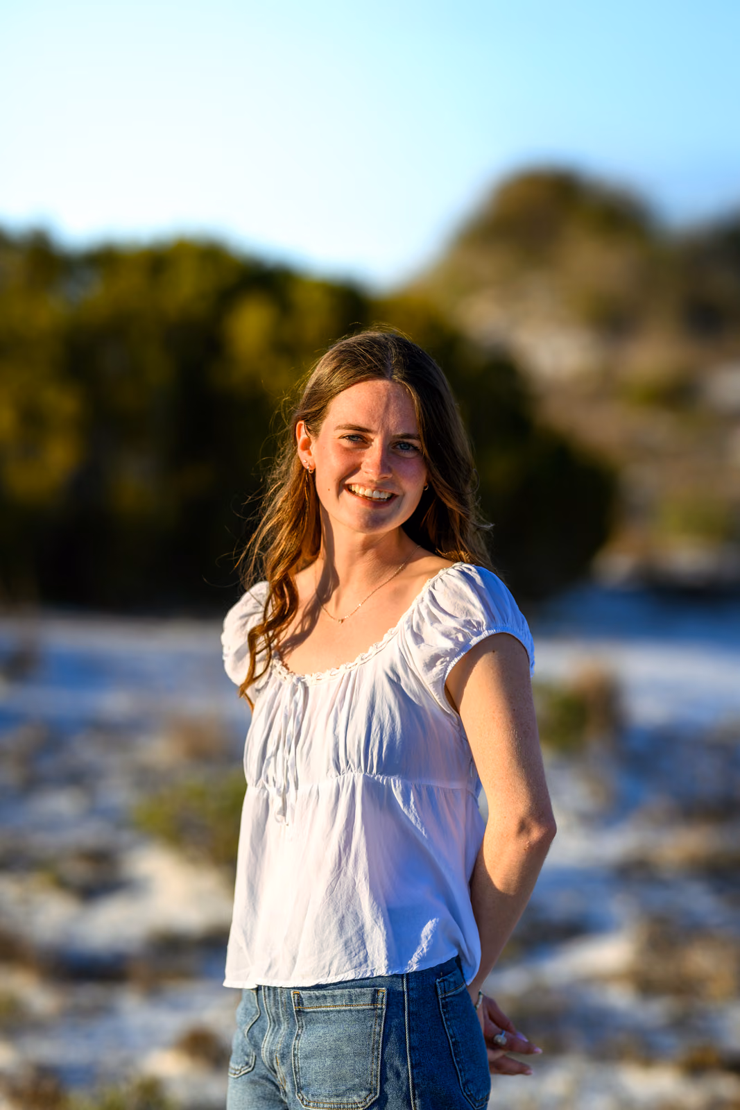 Bailey in a white blouse smiles against softly blurred beach dunes.