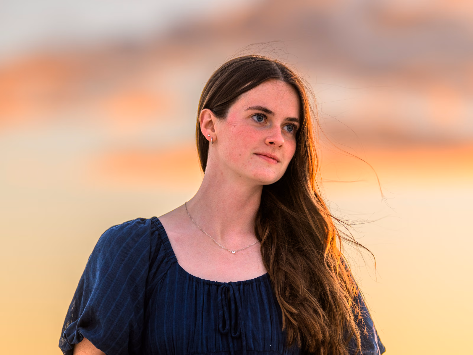 Bailey in a navy dress looking to one side against a softly blurred peach-colored sunset.