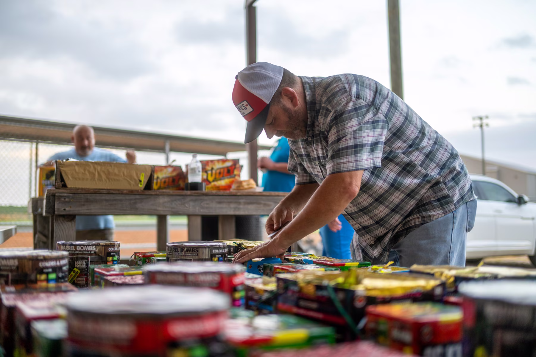 A man arranging fireworks on a table beneath a covered shelter.
