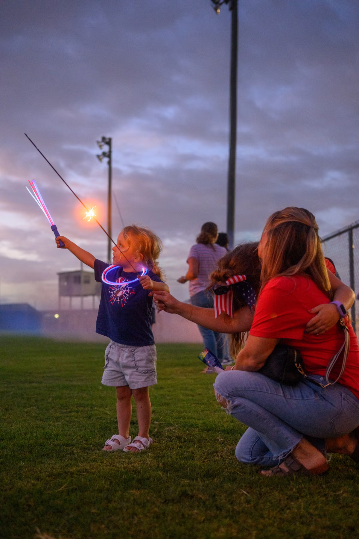 An adult kneeling beside children as they hold sparklers together.
