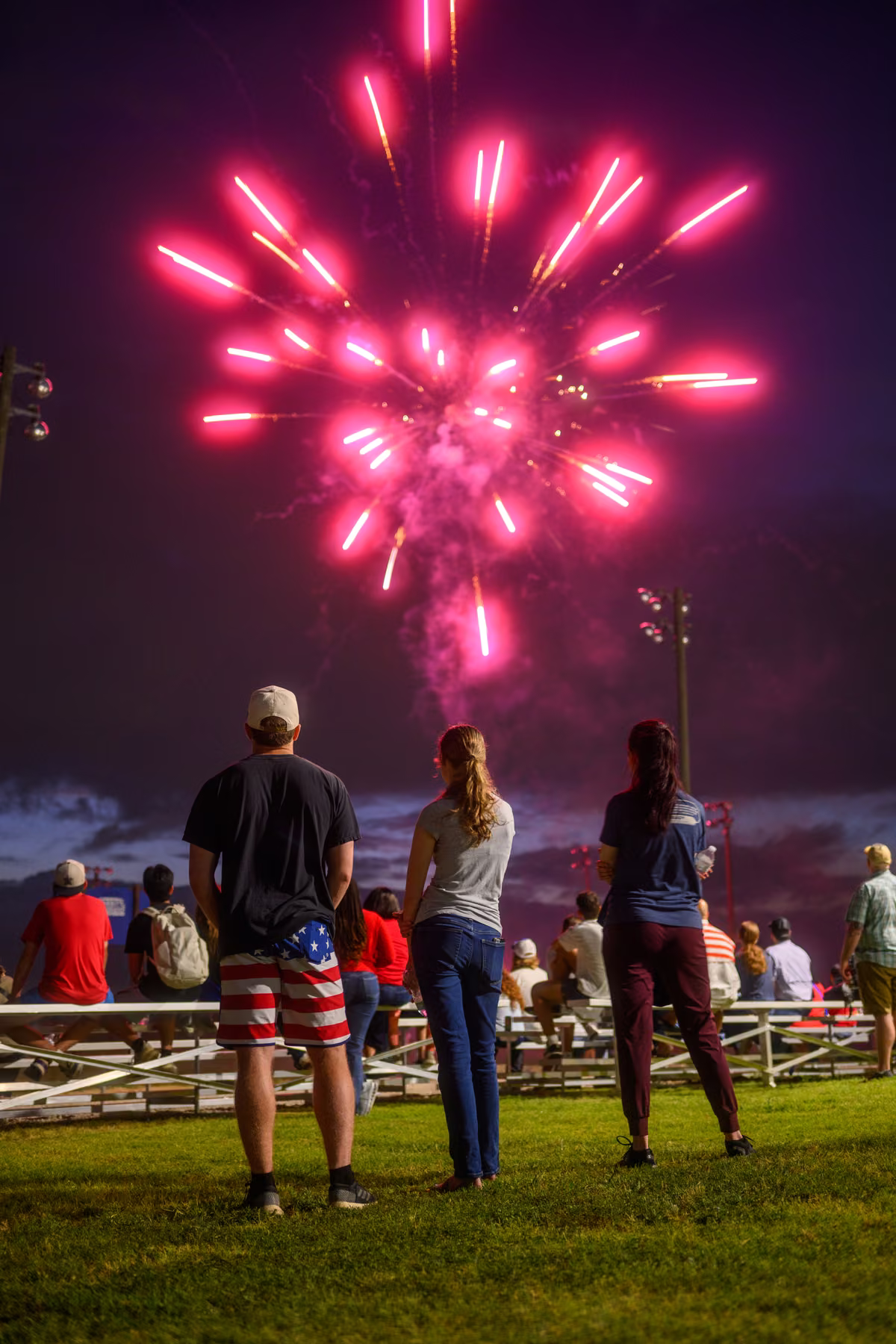 A bright red firework bursting above spectators on the lawn.
