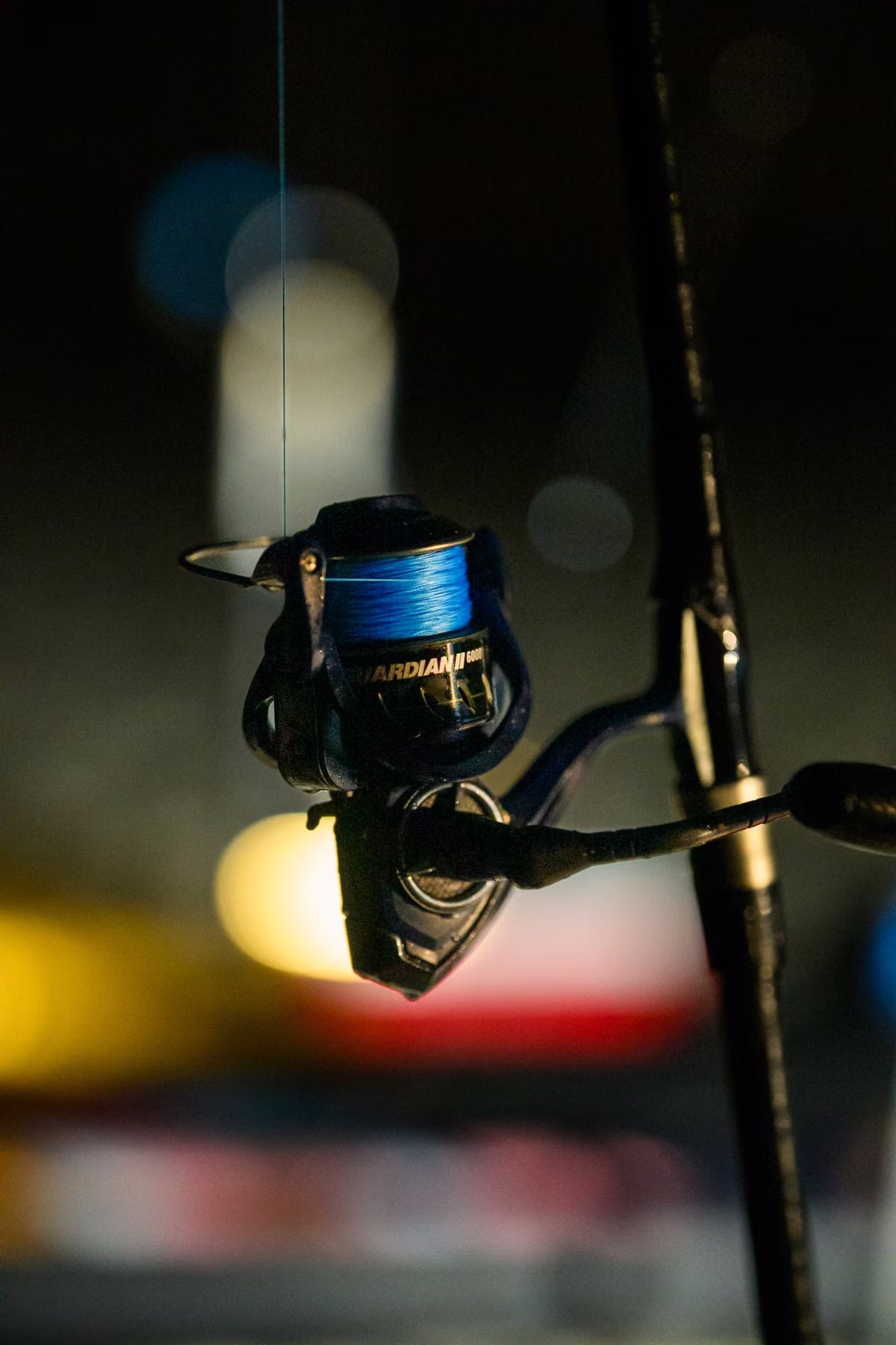 Close-up of a fishing reel with blue line against softly blurred lights at night.