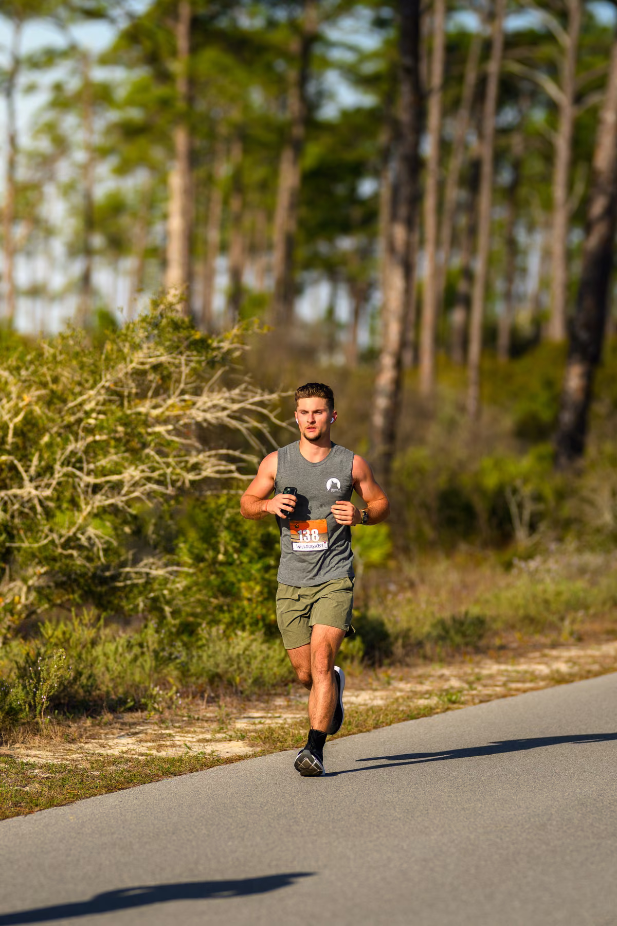 Noah runs along a sunlit road bordered by pine trees and scrub.