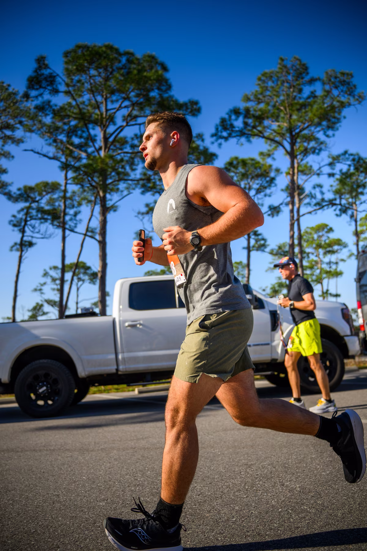 Low-angle view of Noah mid-stride with a blue sky, pine trees and a parked truck behind him.