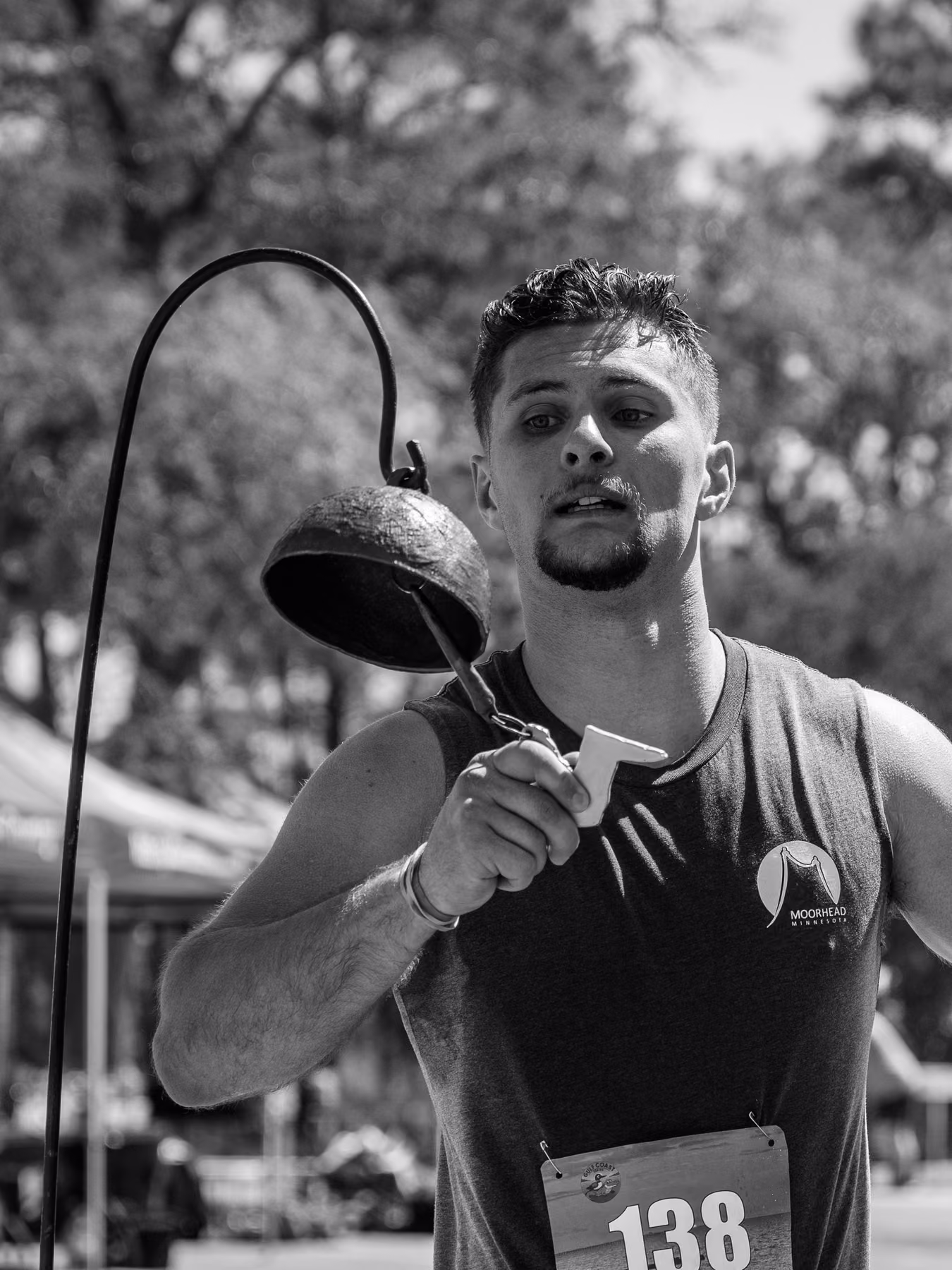 Black-and-white photograph of Noah ringing a metal bell after his run.