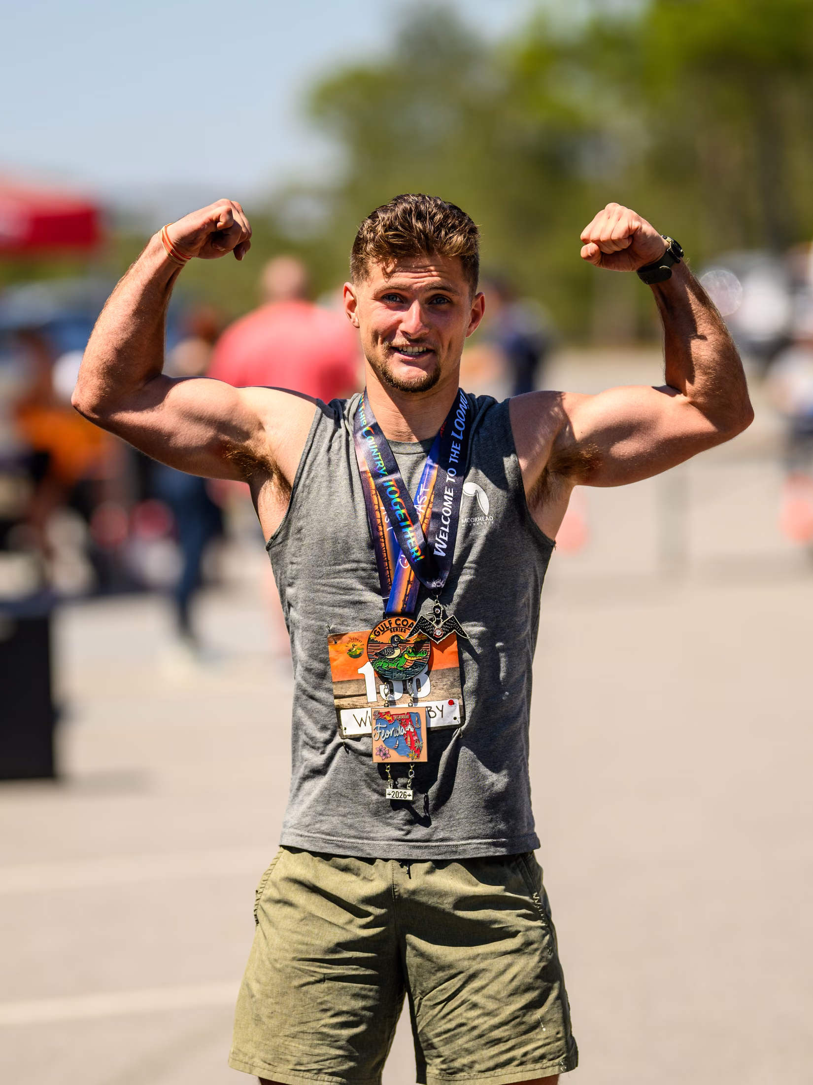 Noah smiles and flexes both arms while wearing his race medals.
